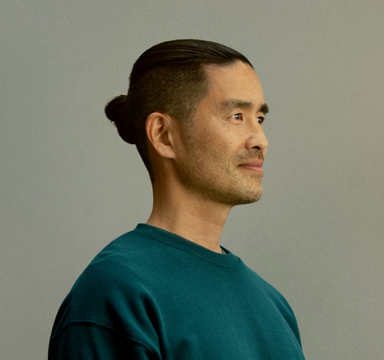 A man in a three-quarter turn with a poised expression against a plain background